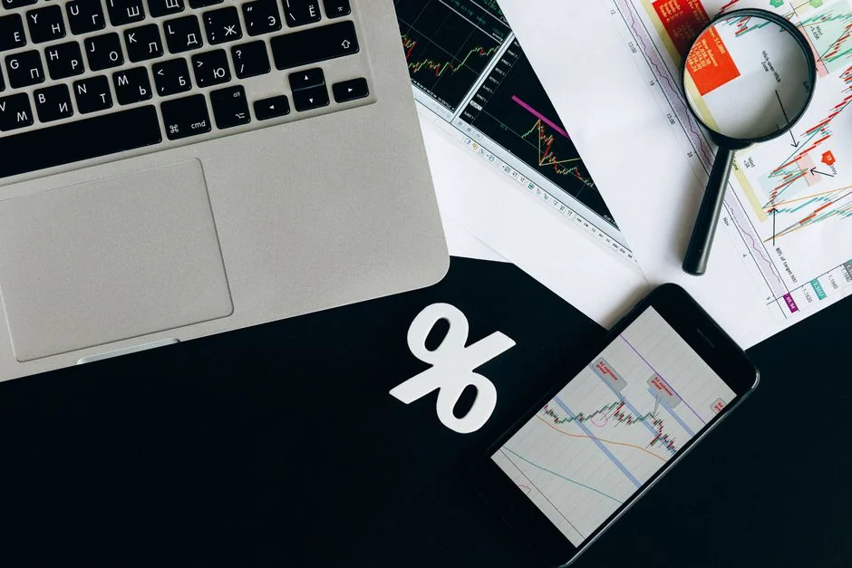 Mains tenant un smartphone avec une application de trading et des graphiques, avec des billets de dollar en arrière-plan.